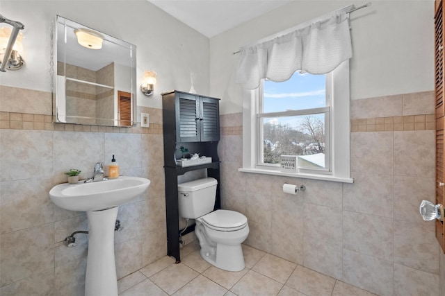 bathroom with toilet, tile patterned floors, tile walls, and sink