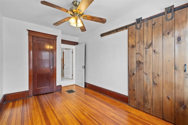 unfurnished bedroom with a barn door, ceiling fan, a closet, and light hardwood / wood-style floors