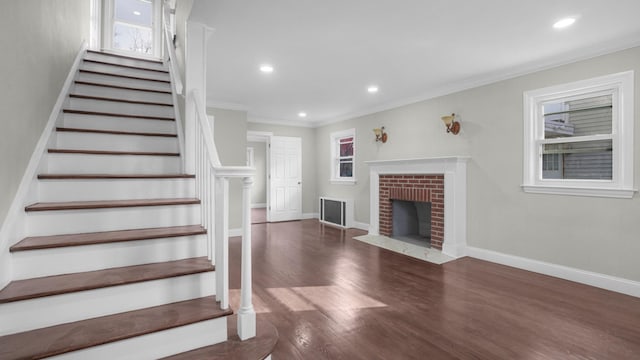 stairs with crown molding, hardwood / wood-style floors, and a brick fireplace