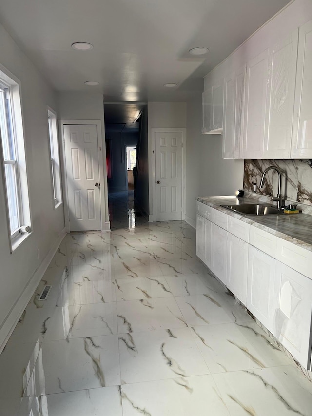 kitchen featuring a healthy amount of sunlight, white cabinetry, sink, and tasteful backsplash