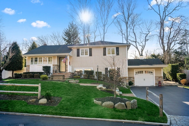 split level home featuring a garage, stone siding, driveway, a chimney, and a front yard