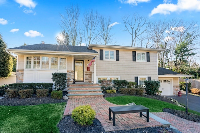 tri-level home featuring aphalt driveway, stone siding, roof with shingles, and an attached garage