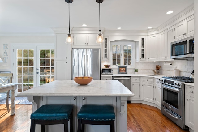 kitchen with appliances with stainless steel finishes, a kitchen island, decorative light fixtures, and white cabinets