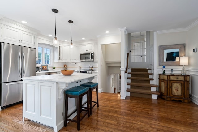 kitchen featuring white cabinets, hanging light fixtures, ornamental molding, appliances with stainless steel finishes, and a center island