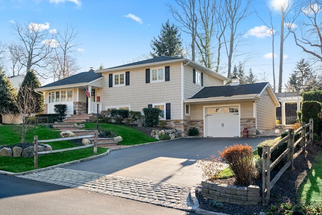 split level home with aphalt driveway, stone siding, a chimney, and an attached garage