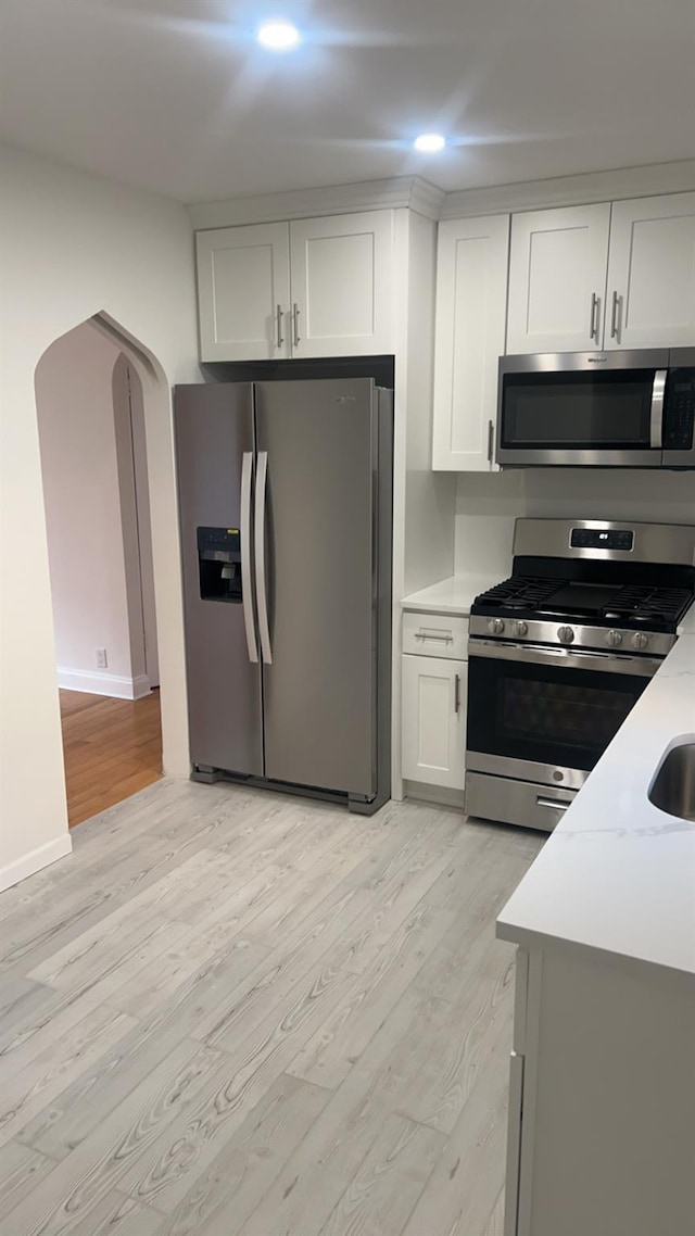 kitchen featuring white cabinetry, sink, light hardwood / wood-style floors, stainless steel appliances, and light stone countertops