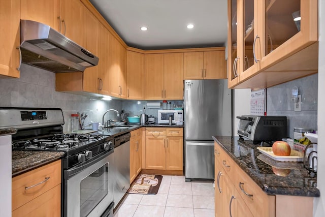 kitchen with dark stone counters, sink, decorative backsplash, light tile patterned flooring, and stainless steel appliances