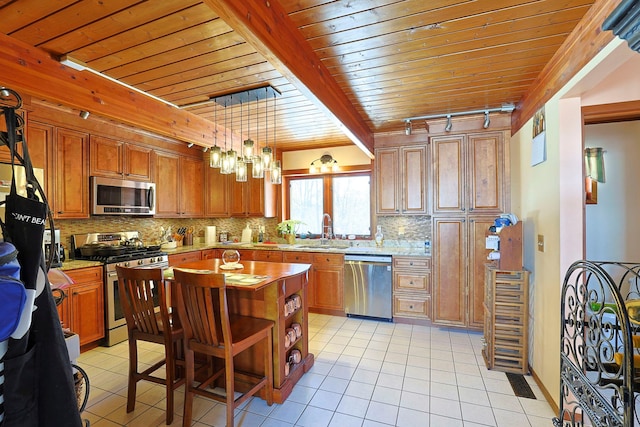 kitchen featuring rail lighting, sink, decorative light fixtures, appliances with stainless steel finishes, and a kitchen island