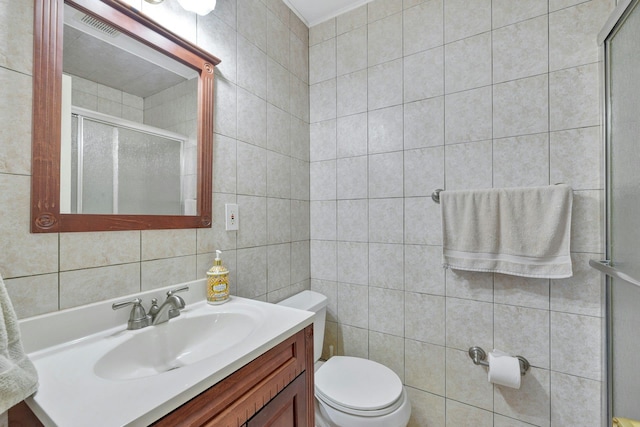 bathroom with an enclosed shower, vanity, toilet, and tile walls