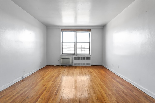 empty room with a wall mounted air conditioner, light wood-type flooring, and radiator