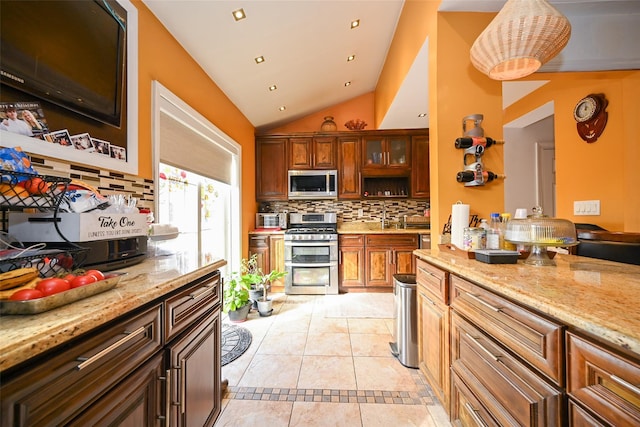 kitchen with light stone counters, lofted ceiling, decorative backsplash, light tile patterned flooring, and appliances with stainless steel finishes