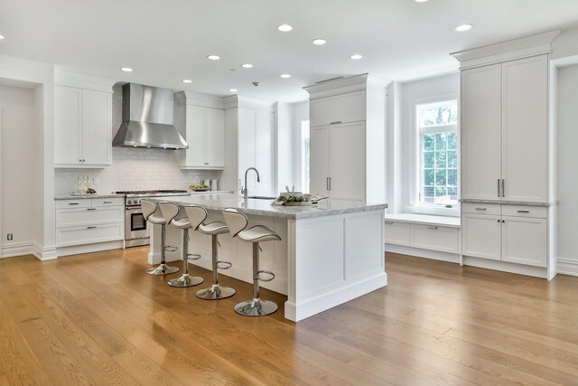 2 Weaver St Unit 3, Scarsdale, NY 10583 - kitchen with white cabinetry, wall chimney exhaust hood, high end stainless steel range oven, an island with sink, and decorative backsplash