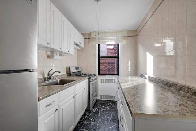 kitchen with stainless steel appliances, white cabinetry, tile walls, and sink