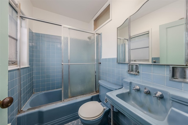 full bathroom with sink, bath / shower combo with glass door, toilet, tile walls, and tasteful backsplash