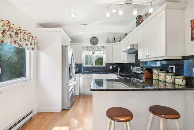 kitchen featuring kitchen peninsula, dark stone counters, stainless steel appliances, baseboard heating, and white cabinets