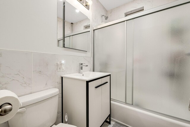 full bathroom featuring combined bath / shower with glass door, vanity, toilet, and tile walls