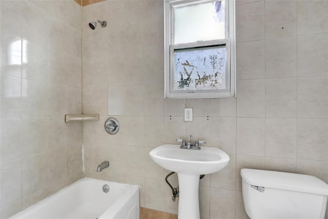 bathroom featuring tiled shower / bath combo, toilet, and tile walls