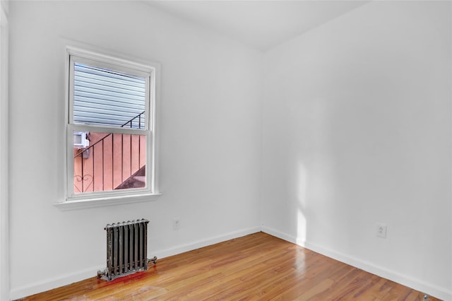 unfurnished room with radiator heating unit, a healthy amount of sunlight, and hardwood / wood-style flooring