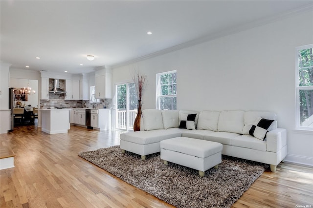 living room with crown molding, a healthy amount of sunlight, a notable chandelier, and light hardwood / wood-style floors