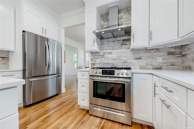 kitchen with white cabinets, wall chimney exhaust hood, light wood-type flooring, and appliances with stainless steel finishes