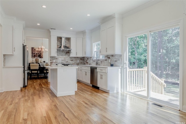 kitchen with light wood-type flooring, wall chimney exhaust hood, stainless steel appliances, white cabinets, and a center island