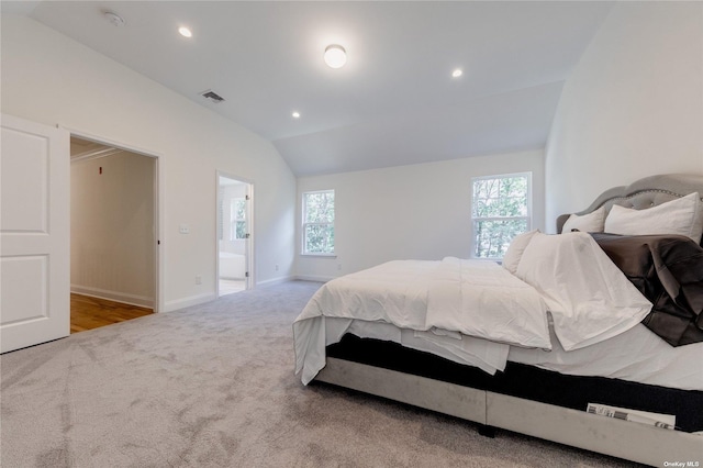 bedroom with connected bathroom, multiple windows, light colored carpet, and lofted ceiling