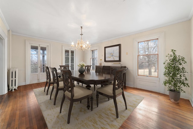 dining room featuring radiator heating unit, hardwood / wood-style floors, crown molding, and a notable chandelier