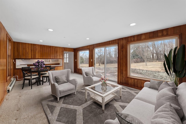 carpeted living room featuring a baseboard heating unit, wood walls, and a healthy amount of sunlight