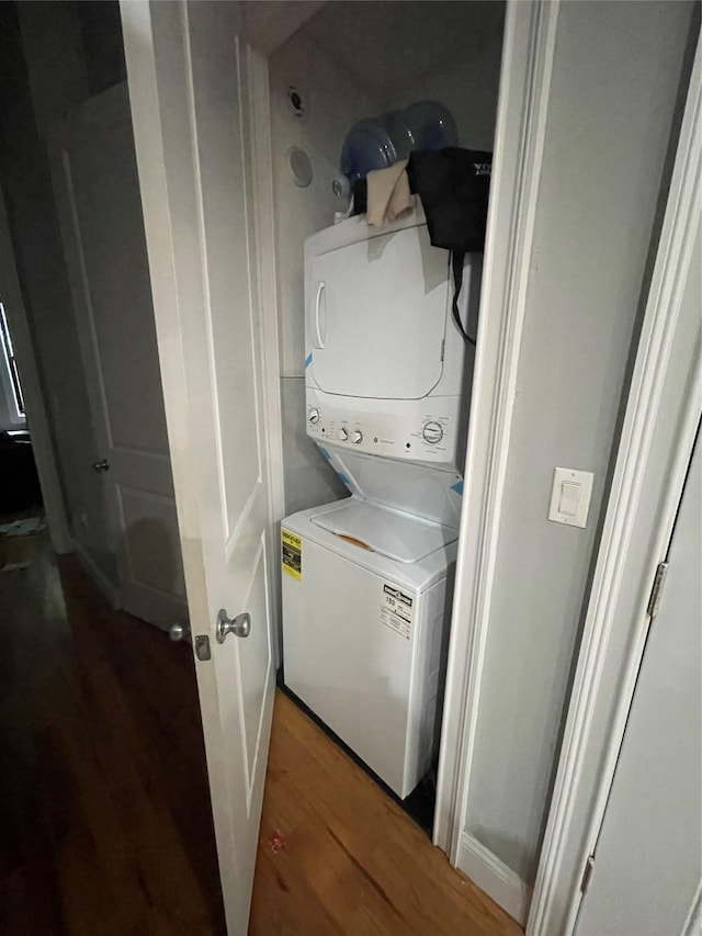 laundry area with dark wood-type flooring and stacked washing maching and dryer