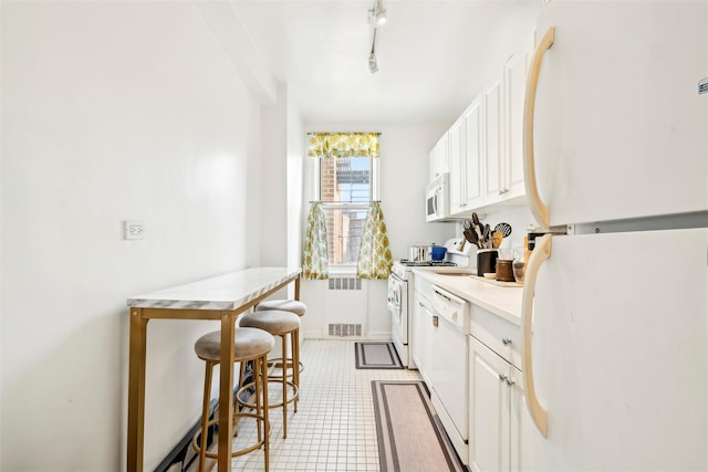 5635 Netherland Ave Unit 4E, Bronx, NY 10471 - kitchen featuring radiator, a kitchen breakfast bar, white appliances, and white cabinetry