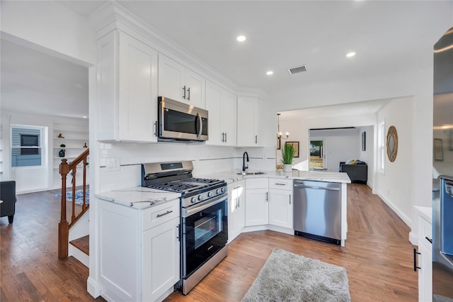 kitchen featuring kitchen peninsula, stainless steel appliances, sink, white cabinets, and light hardwood / wood-style floors