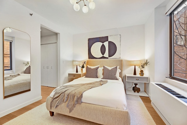 bedroom featuring a closet, radiator heating unit, wood-type flooring, and an inviting chandelier