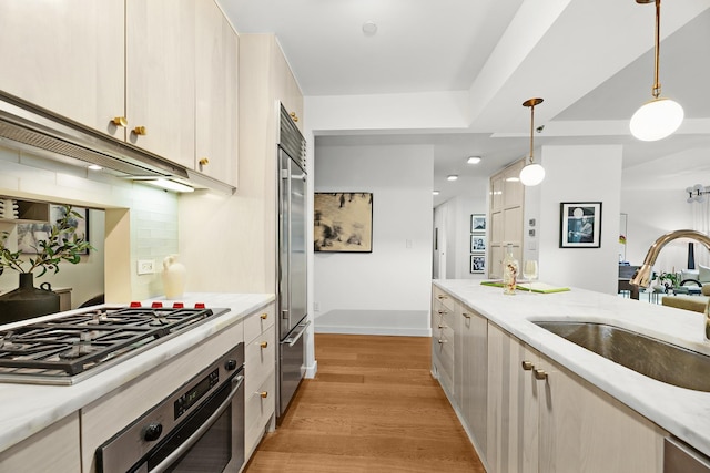 kitchen with backsplash, stainless steel appliances, sink, decorative light fixtures, and light hardwood / wood-style floors