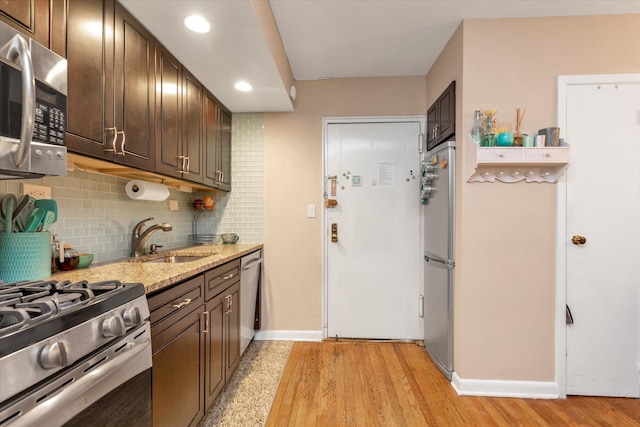 kitchen with sink, light stone countertops, appliances with stainless steel finishes, tasteful backsplash, and dark brown cabinets