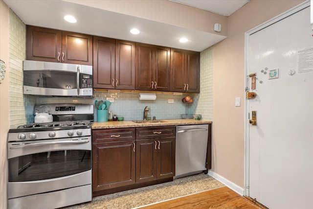 kitchen featuring sink, light stone counters, decorative backsplash, dark brown cabinets, and appliances with stainless steel finishes