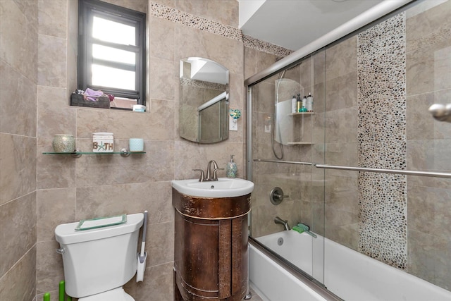 full bathroom featuring vanity, toilet, shower / bath combination with glass door, and tile walls