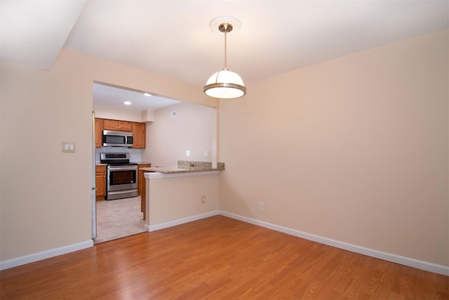 kitchen featuring pendant lighting, kitchen peninsula, stainless steel appliances, and light wood-type flooring