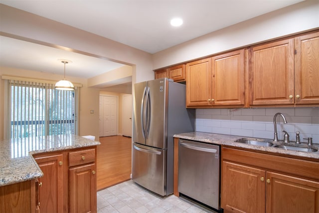 kitchen with light stone countertops, sink, decorative light fixtures, backsplash, and stainless steel appliances