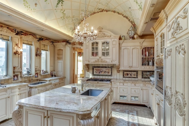 kitchen featuring light stone countertops, sink, hanging light fixtures, cream cabinetry, and a kitchen island with sink