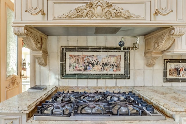 room details with stainless steel gas stovetop, light stone countertops, backsplash, and cream cabinets