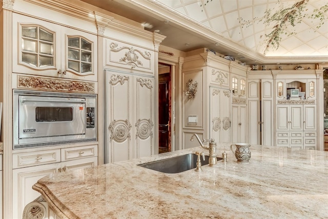 kitchen with light stone countertops, cream cabinets, stainless steel microwave, and sink
