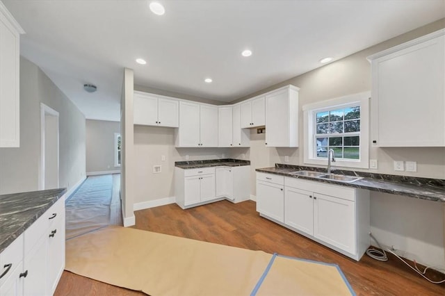 kitchen with white cabinets, dark stone countertops, sink, and hardwood / wood-style flooring