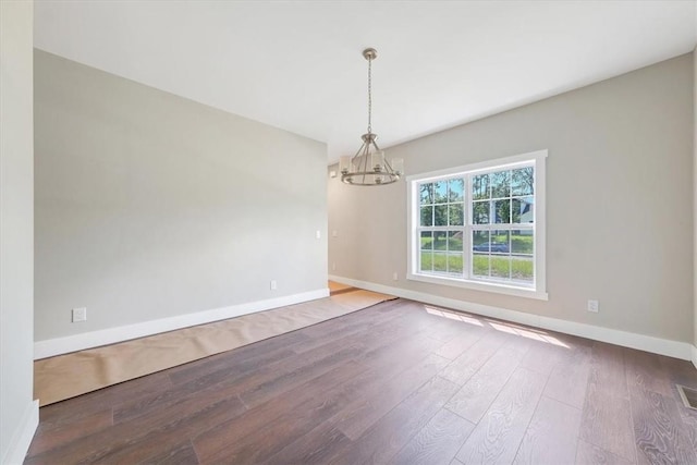 empty room featuring wood-type flooring and an inviting chandelier