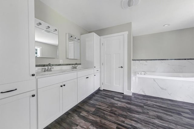 bathroom featuring a relaxing tiled tub, wood-type flooring, and vanity