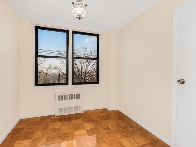 spare room featuring radiator, a wealth of natural light, light parquet floors, and a notable chandelier