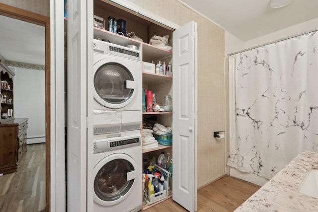 clothes washing area featuring a baseboard radiator, light hardwood / wood-style flooring, and stacked washer and clothes dryer