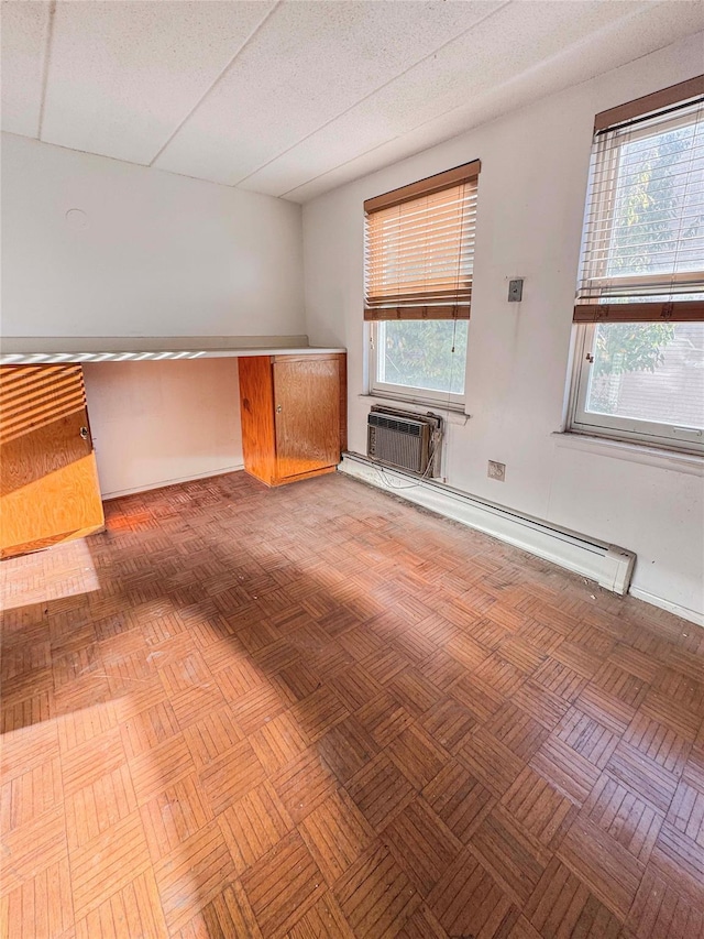 unfurnished living room featuring a wall mounted air conditioner, light parquet flooring, a drop ceiling, and a baseboard heating unit