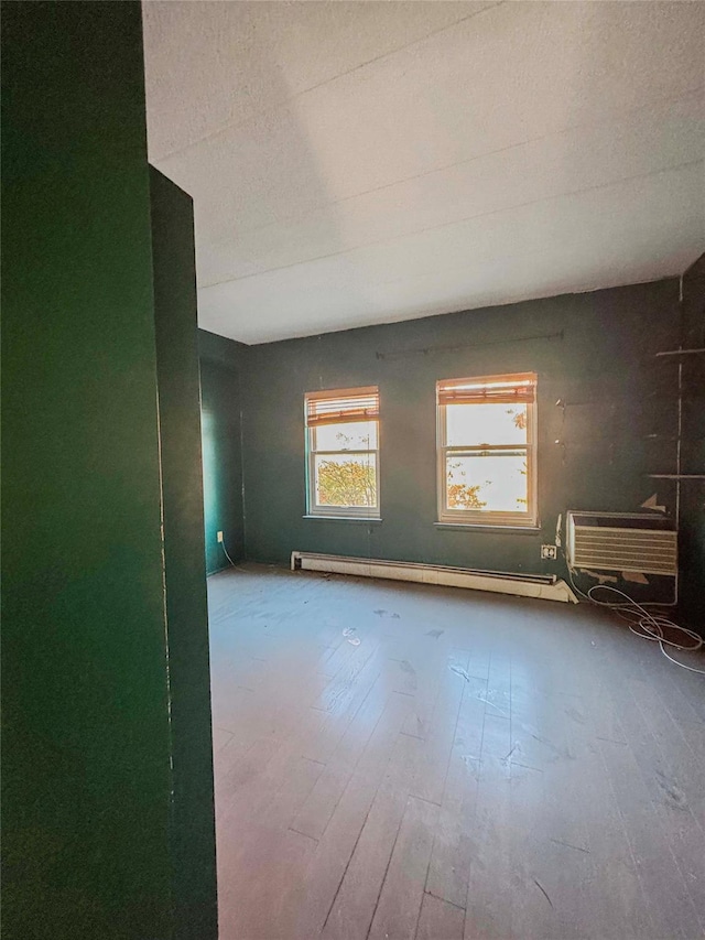 unfurnished room featuring hardwood / wood-style floors, a baseboard radiator, and an AC wall unit