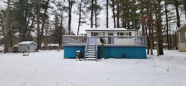 snow covered back of property featuring a storage unit and a wooden deck