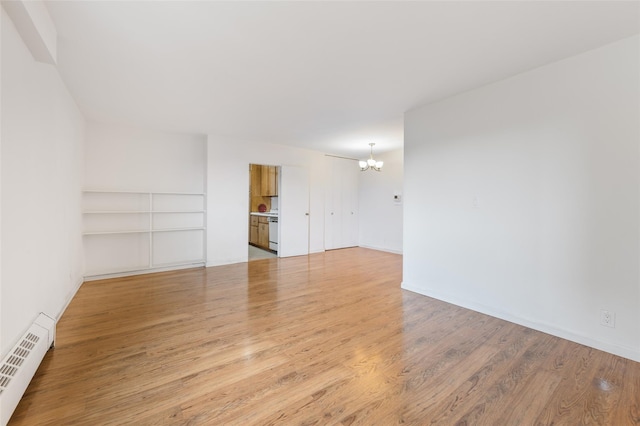 empty room featuring an inviting chandelier, light hardwood / wood-style flooring, and a baseboard heating unit